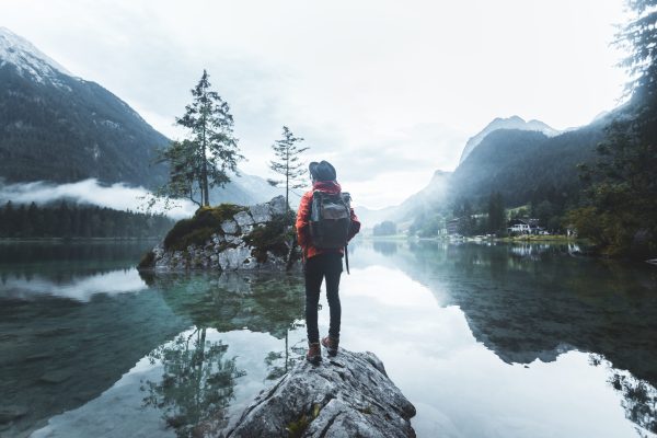 Man wearing a hat with backpack hiking Lifestyle adventure concept forest and lake on background active vacations into the wild